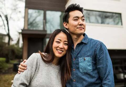 A couple smiles in front of a house.